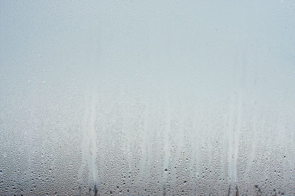 Heavy condensation forming on cold window glass surface indoors