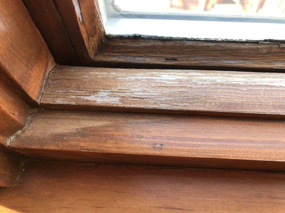 Weathered wooden window frame showing peeling finish and surface damage